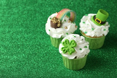 Photo of St. Patrick's day party. Tasty festively decorated cupcakes on shiny green surface, closeup. Space for text