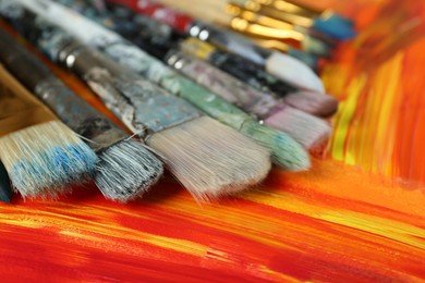 Photo of Set of different brushes on abstract colorful paint, closeup