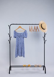 Rack with accessories and stylish women`s dress on wooden hanger against light grey background
