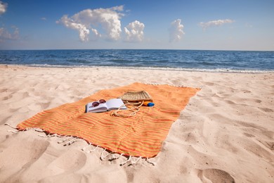 Photo of Orange striped beach towel with bag, accessories and book on sandy seashore