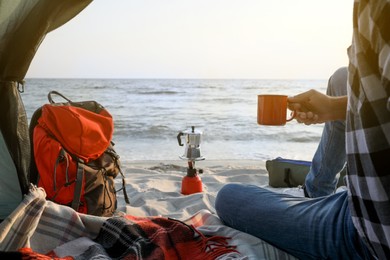 Man with cup of hot drink in camping tent, closeup