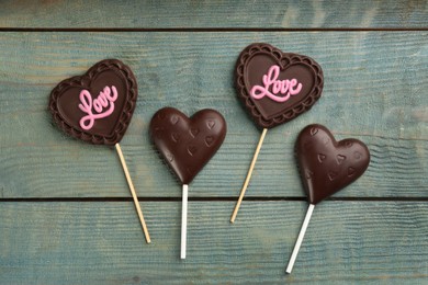 Photo of Different chocolate heart shaped lollipops on light blue wooden table, flat lay