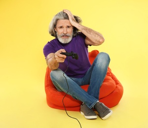 Emotional mature man playing video games with controller on color background