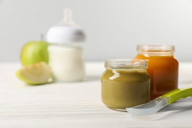 Jars with healthy baby food and spoon on white wooden table. Space for text