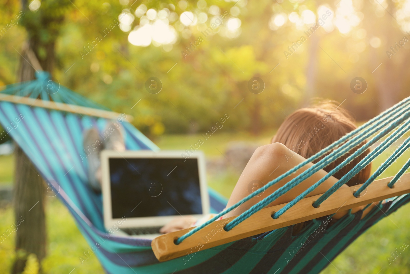 Photo of Young woman with laptop resting in comfortable hammock at green garden