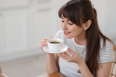 Smiling woman drinking coffee at breakfast on blurred background. Space for text