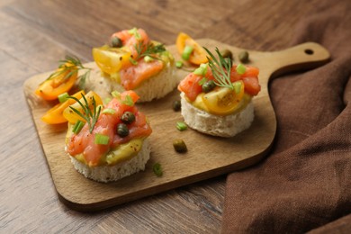 Tasty canapes with salmon served on wooden table, closeup
