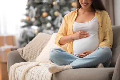 Photo of Happy pregnant woman on sofa in living room decorated for Christmas, closeup. Expecting baby