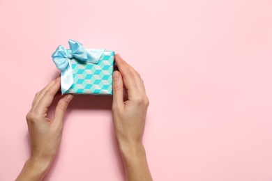 Woman holding Christmas gift on pink background, top view. Space for text