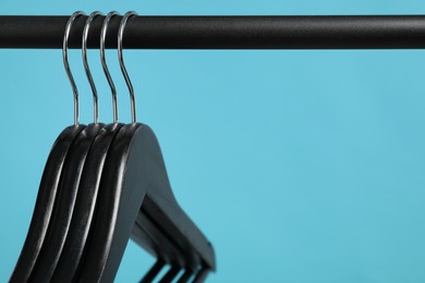 Photo of Black clothes hangers on rack against light blue background, closeup. Space for text