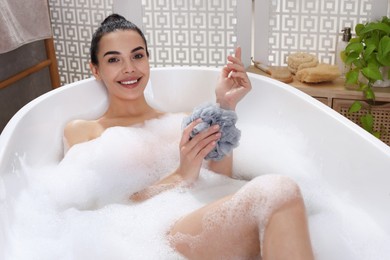 Photo of Woman taking bath with mesh pouf indoors