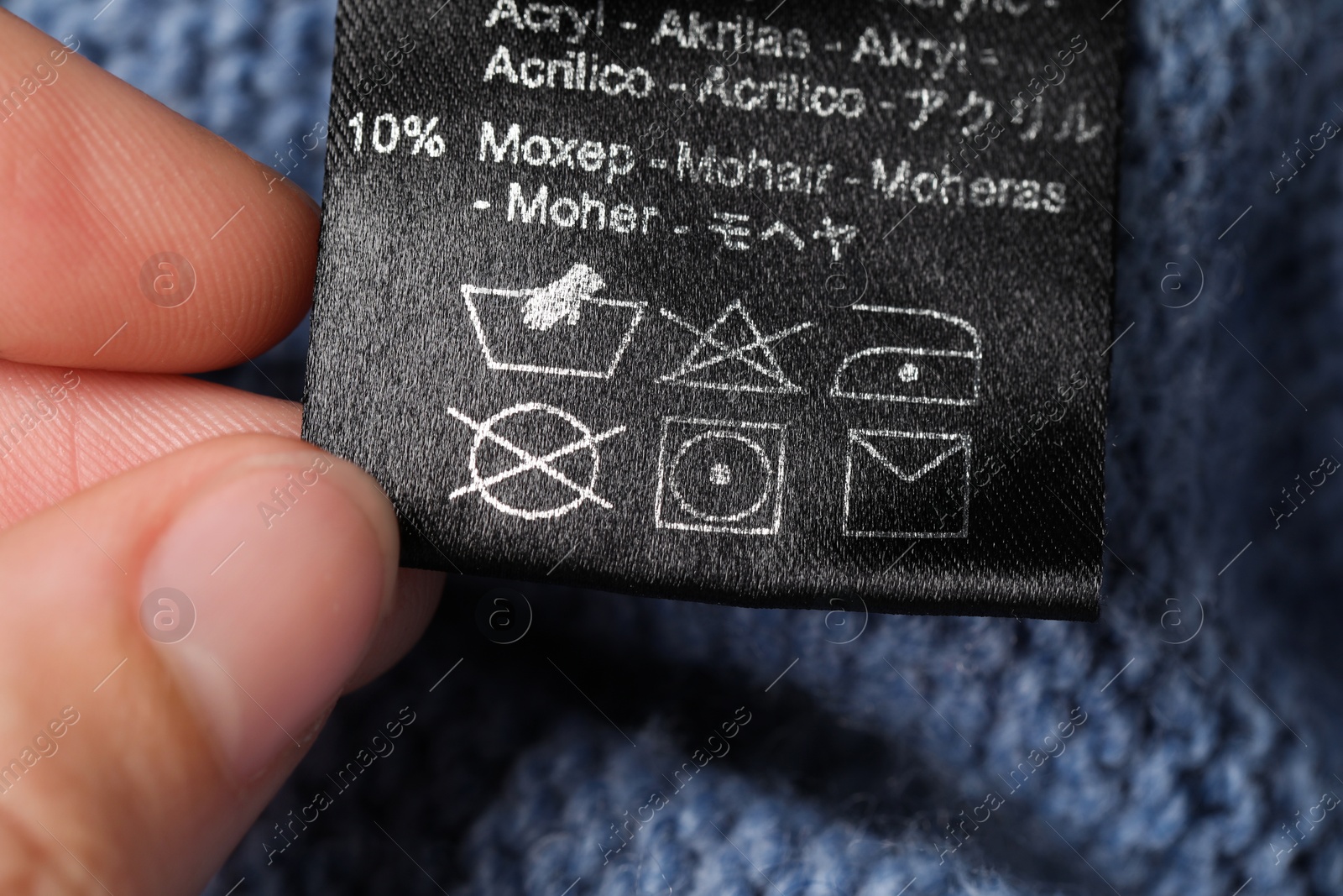 Photo of Woman holding clothing label on blue knitted garment, closeup