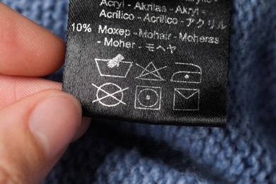 Woman holding clothing label on blue knitted garment, closeup