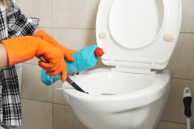 Photo of Woman in protective gloves cleaning toilet bowl with brush in bathroom, closeup