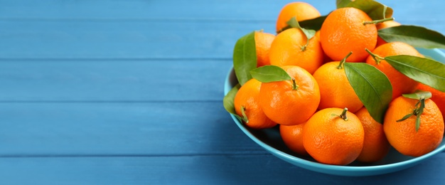 Fresh ripe tangerines with green leaves on blue wooden table, closeup