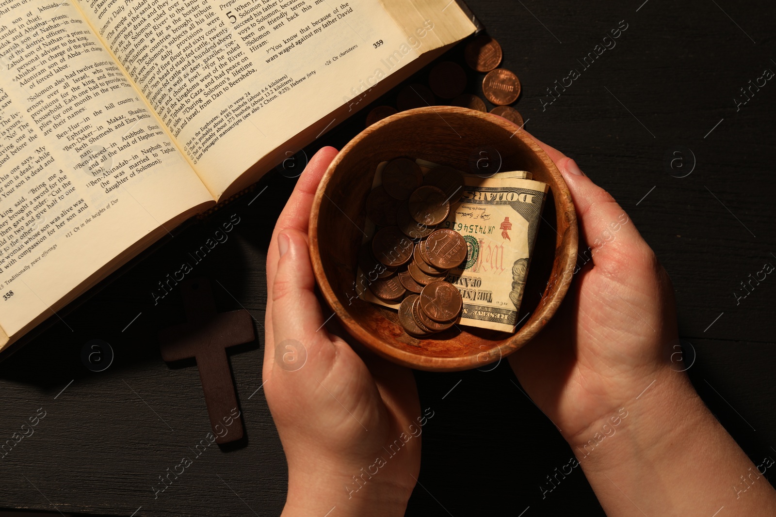 Photo of Donate and give concept. Woman with bowl of money, closeup. Bible and cross on black wooden table, top view