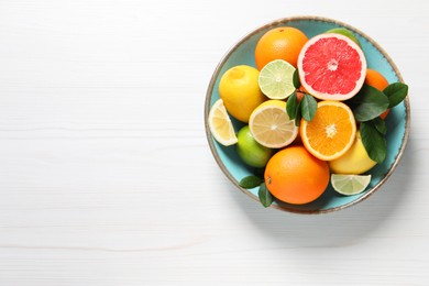 Photo of Different cut and whole citrus fruits on white wooden table, top view. Space for text