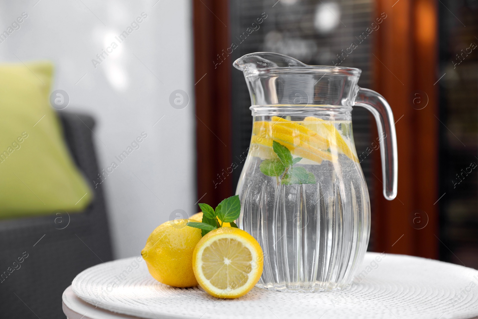 Photo of Jug of water with lemons and mint on white table outdoors