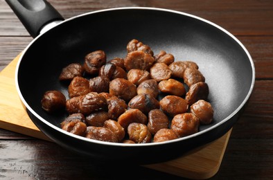 Roasted edible sweet chestnuts in frying pan on wooden table, closeup