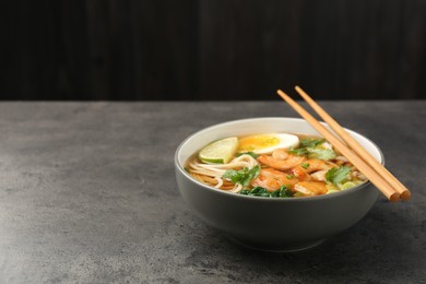 Photo of Delicious ramen with shrimps and chopsticks on grey table, space for text. Noodle soup