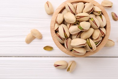 Tasty pistachios in bowl on white wooden table, top view. Space for text