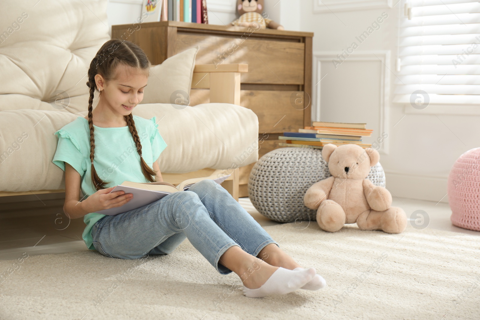 Photo of Cute little girl reading book on floor at home