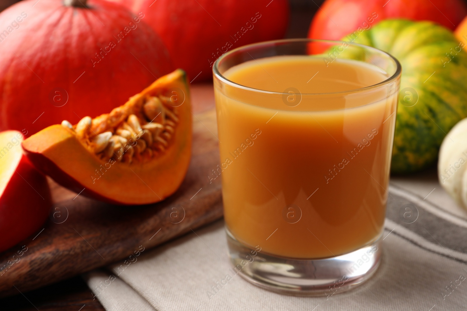 Photo of Tasty pumpkin juice in glass and different pumpkins on wooden table, closeup