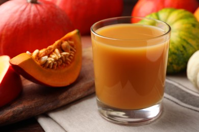 Tasty pumpkin juice in glass and different pumpkins on wooden table, closeup
