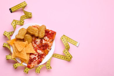 Photo of Chips, chicken nuggets, pizza and measuring tape on pink background, flat lay and space for text. Diet concept