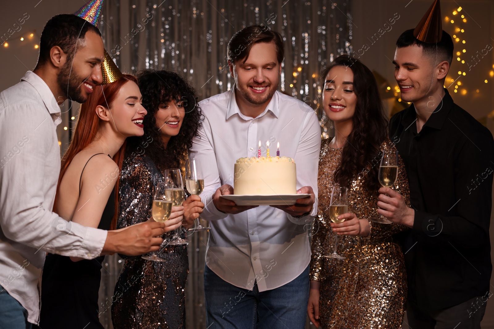 Photo of Happy friends with tasty cake and glasses of sparkling wine celebrating birthday indoors