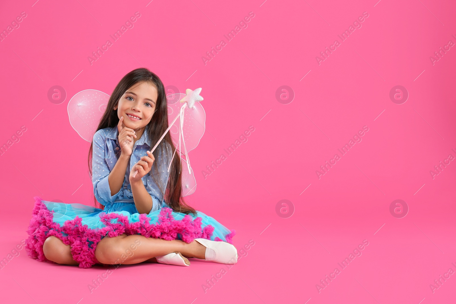 Photo of Cute little girl in fairy costume with wings and magic wand on pink background. Space for text