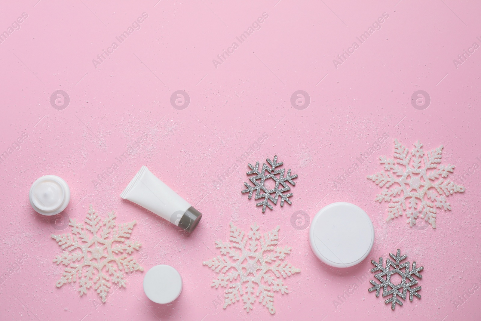 Photo of Flat lay composition with cosmetic products and snowflakes on pink background, space for text. Winter skin care