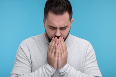 Sick man coughing on light blue background