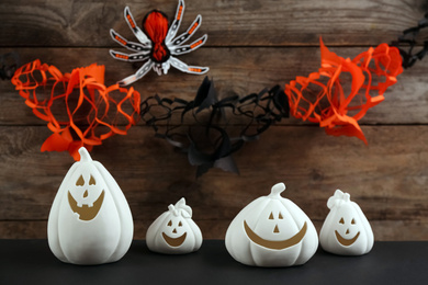 White pumpkin shaped candle holders on black table against wooden wall with paper spider and garland. Halloween decoration