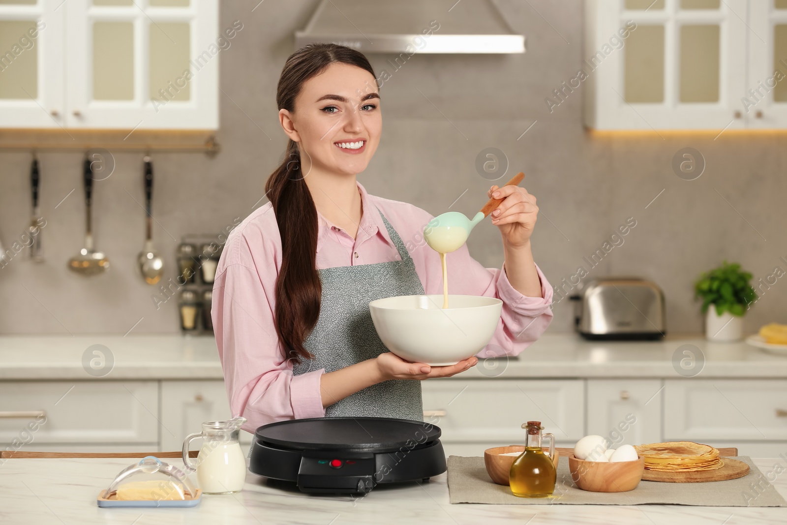 Photo of Happy woman with dough for crepes at white marble table in kitchen