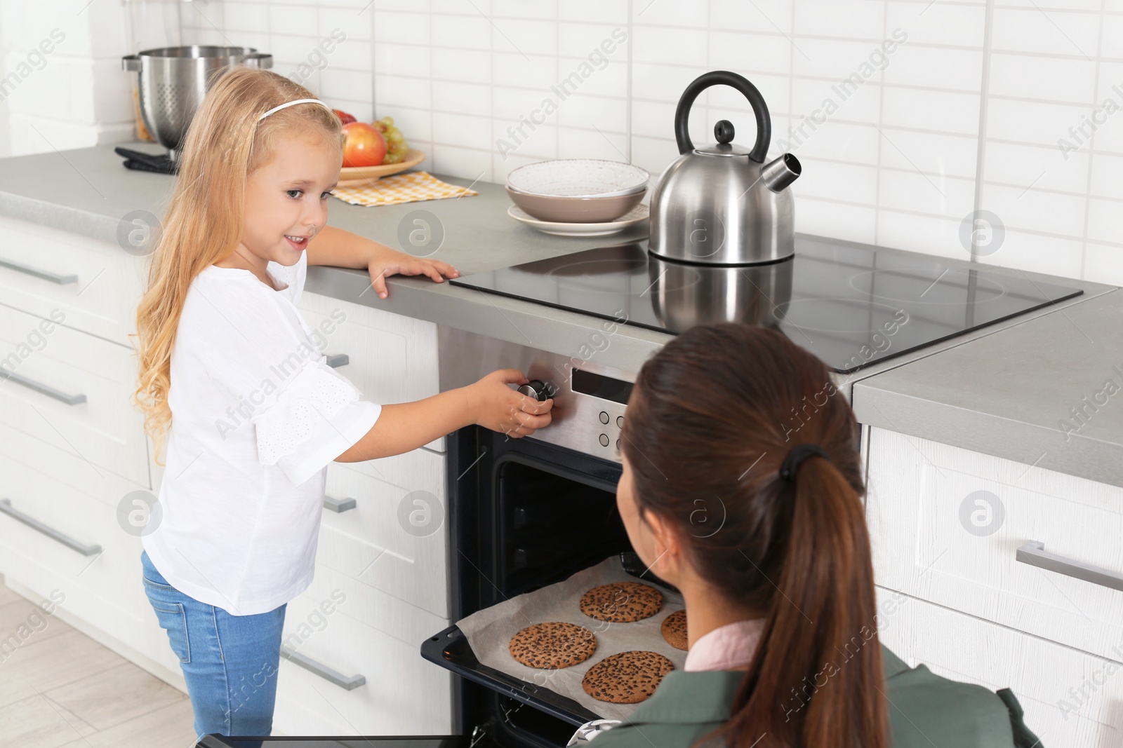 Photo of Young woman and her daughter baking cookies in oven at home