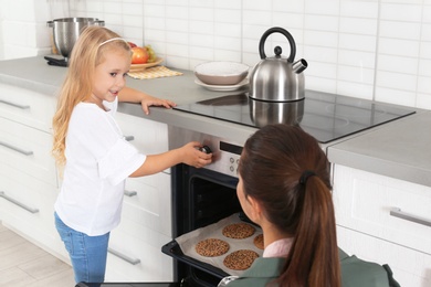 Young woman and her daughter baking cookies in oven at home