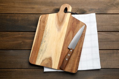 Photo of Cutting board, towel and knife on wooden table, top view. Cooking utensil