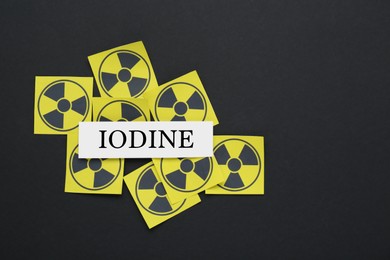 Photo of Paper note with word Iodine and radiation signs on black background, flat lay. Space for text