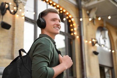 Photo of Smiling man in headphones listening to music outdoors. Space for text