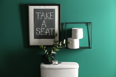 Decor elements, paper rolls and toilet bowl near green wall. Bathroom interior