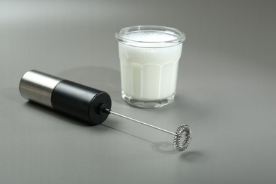 Photo of Mini mixer (milk frother) and whipped milk in glass on grey background