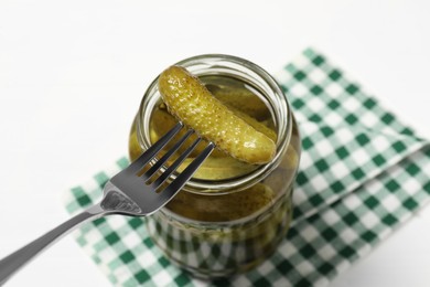 Fork with pickled cucumber over jar on white table, above view