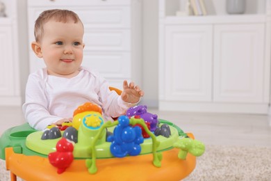 Portrait of cute baby with toy walker at home, space for text. Learning to walk