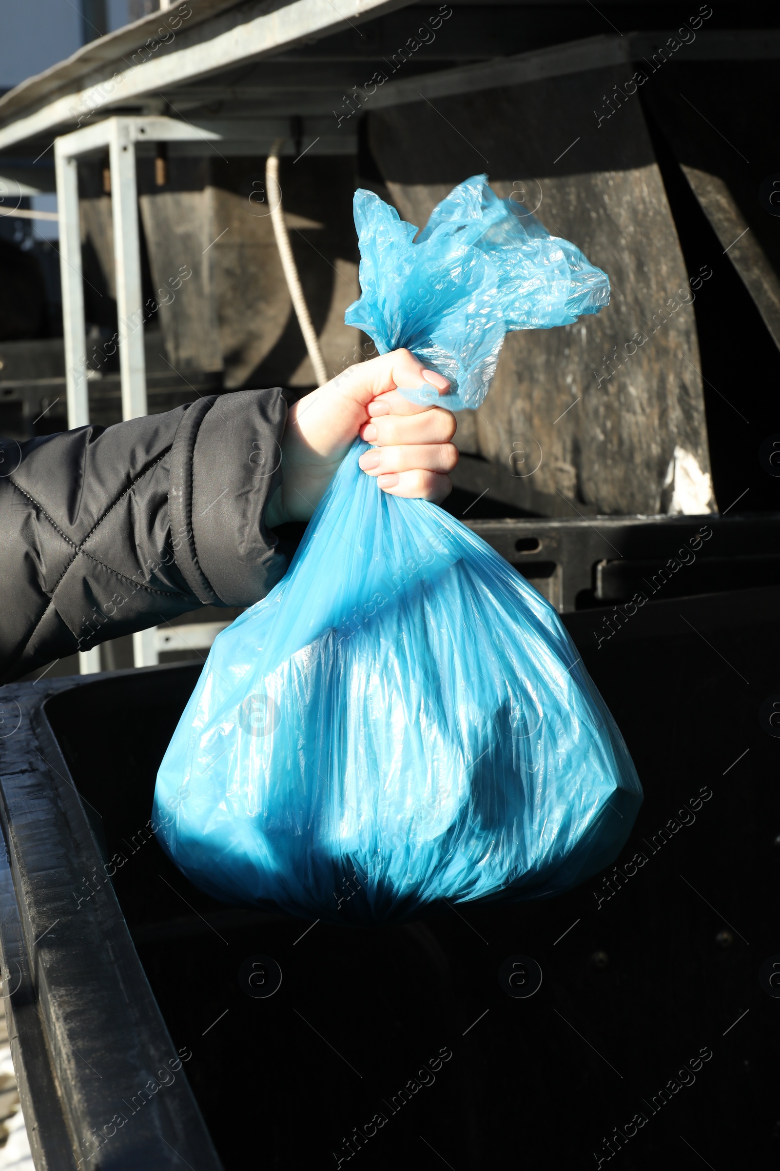 Photo of Woman throwing trash bag full of garbage in bin outdoors, closeup