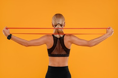 Photo of Woman exercising with elastic resistance band on orange background, back view