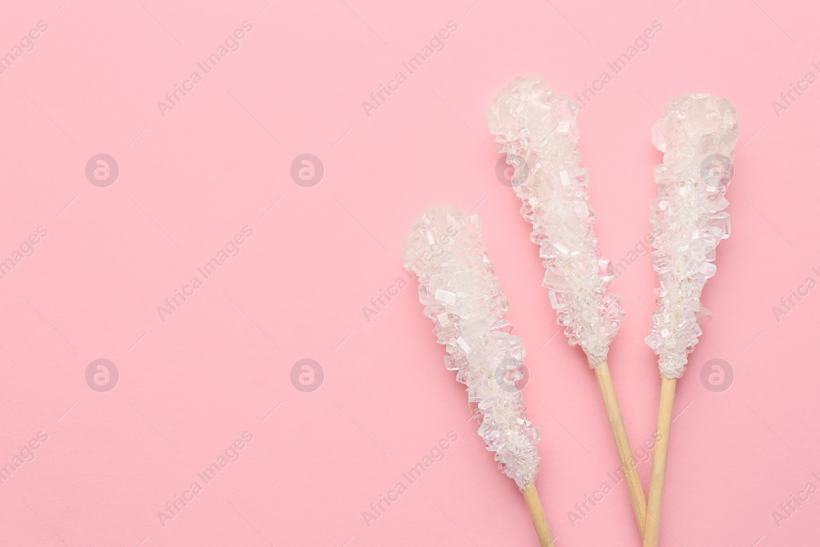 Photo of Wooden sticks with sugar crystals and space for text on pink background, flat lay. Tasty rock candies