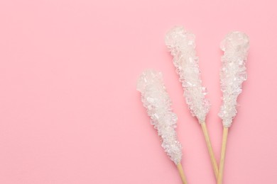Photo of Wooden sticks with sugar crystals and space for text on pink background, flat lay. Tasty rock candies