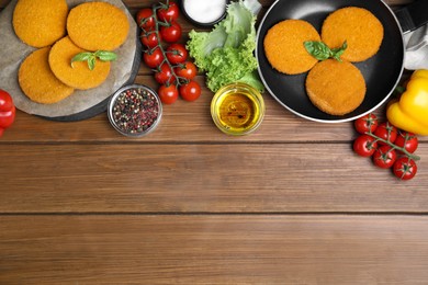 Photo of Delicious fried breaded cutlets, spices and vegetables on wooden table, flat lay. Space for text