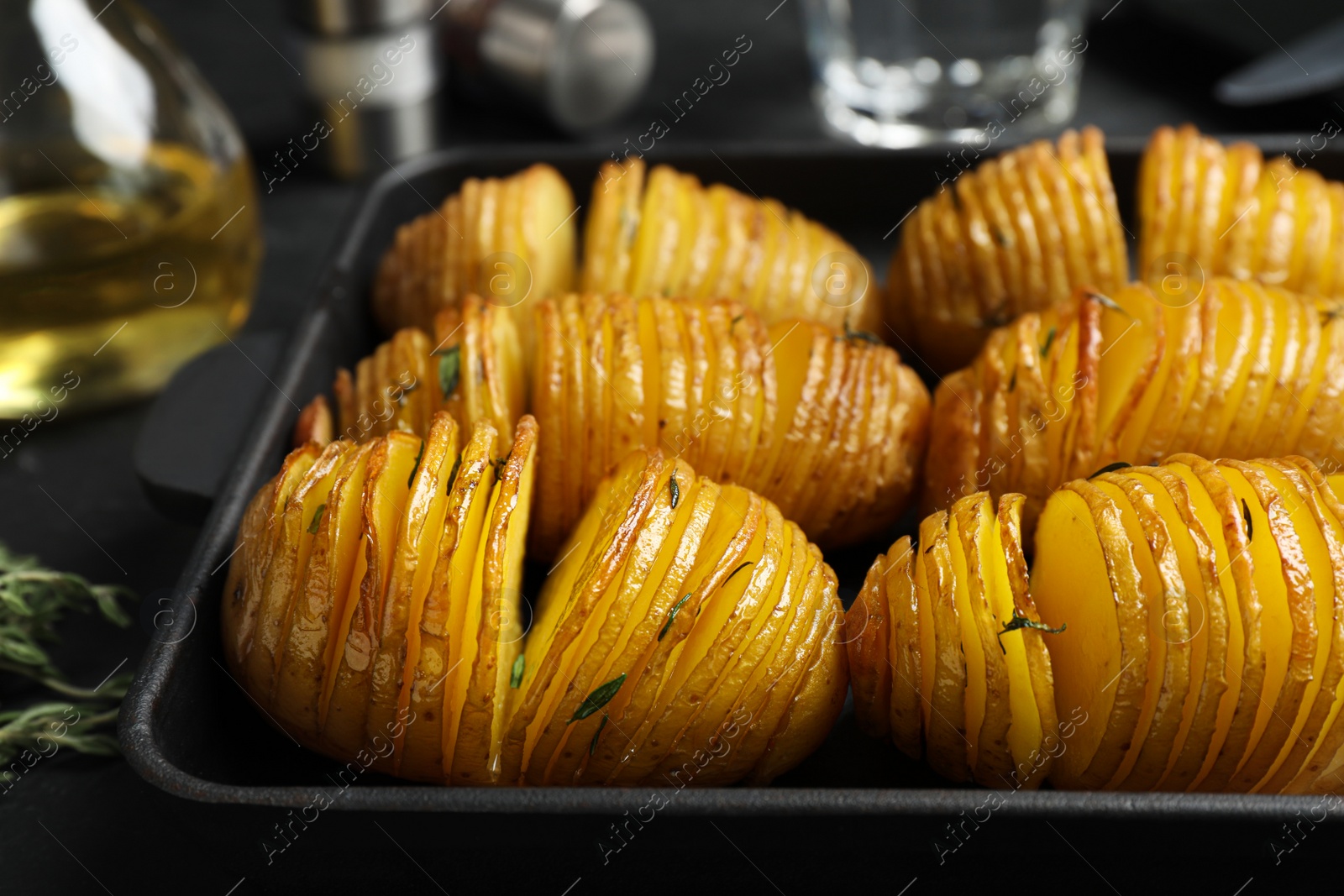 Photo of Delicious homemade Hasselback potatoes in baking pan on black table, closeup